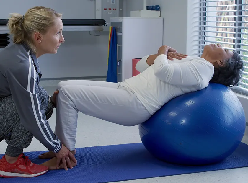 a physiotherapy session where the therapist is helping a patient use a workout ball